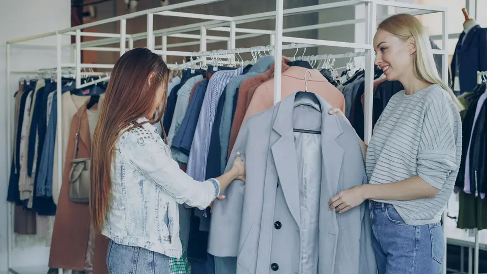 Boutique owner showing a shopper a coat among clothing racks